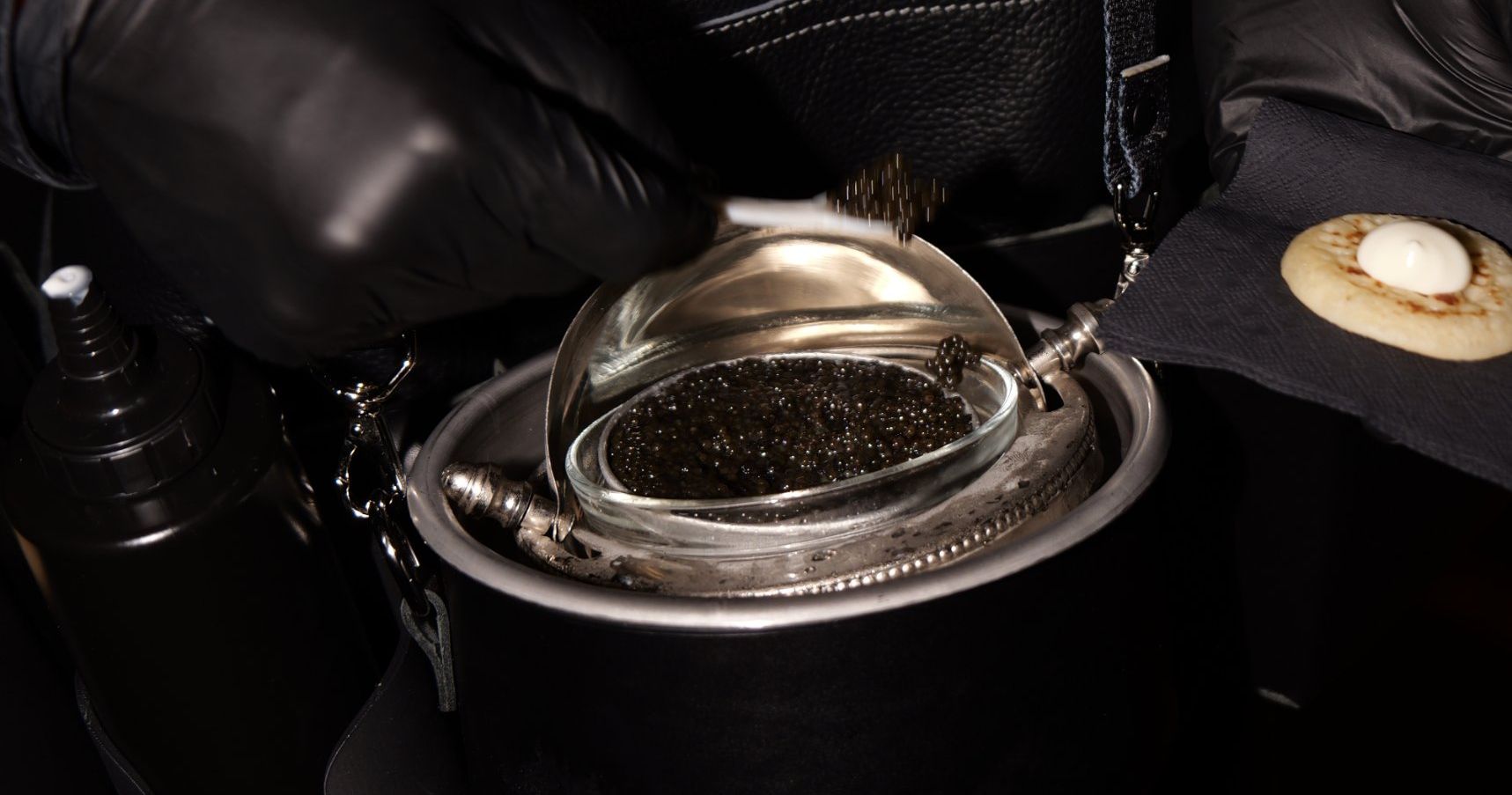 Main gantée prenant le caviar dans la ceinture de dégustation, blini prêt à côté